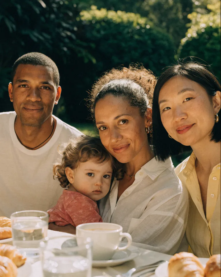 Brunch entre amis au jardin : les adultes sont visibles, le visage du tout-petit est masqué par un smiley.
