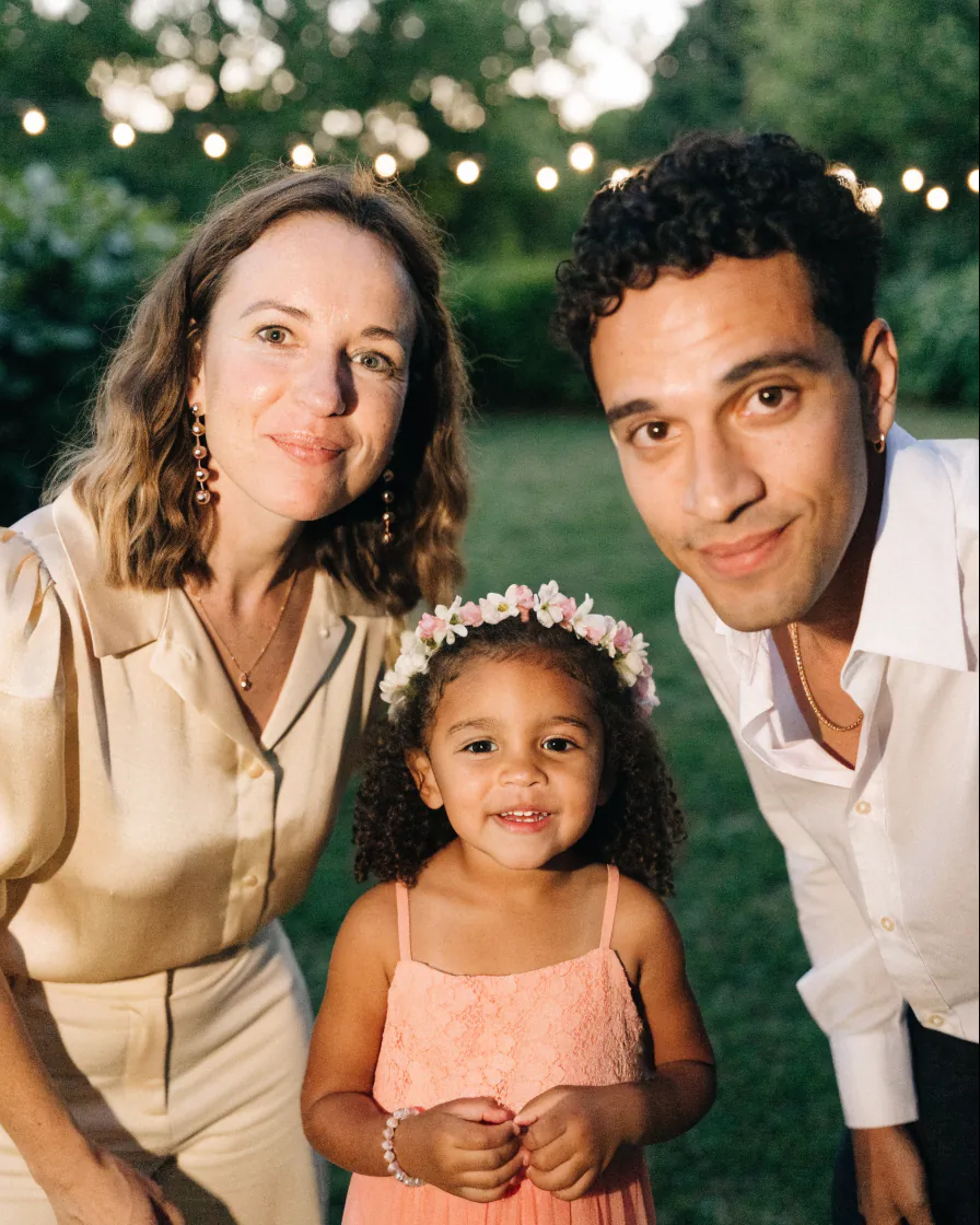 Deux invités d'un mariage avec une petite fille, dont le visage est masqué par une fleur.